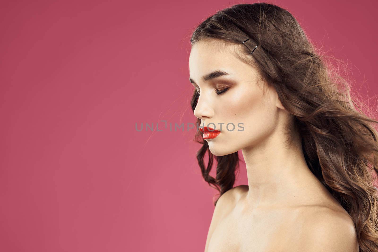Beautiful brunette woman with makeup on her face on a pink background naked shoulders. High quality photo