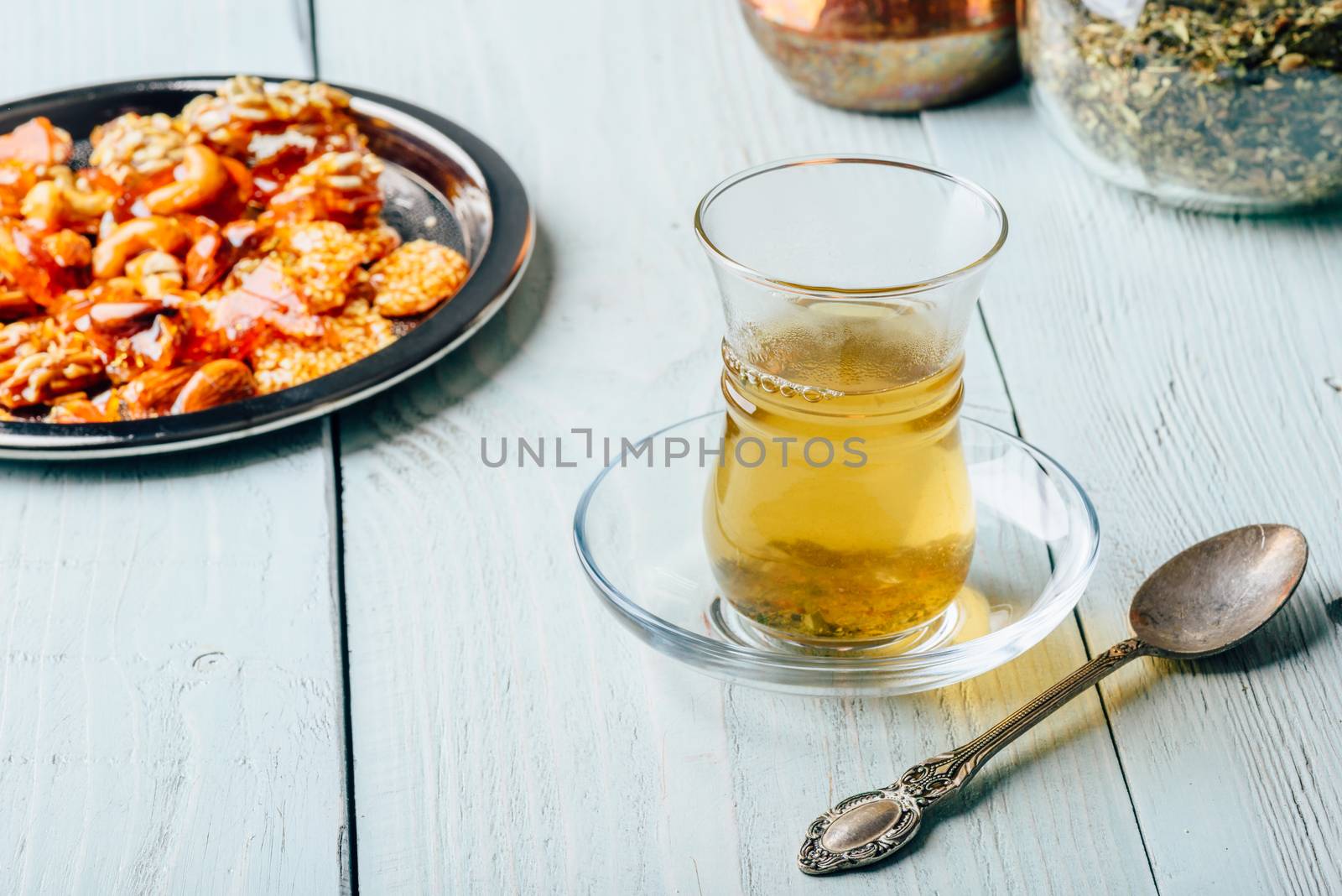 Herbal tea in armudu glass with oriental nut delights on metal plate over light wooden surface