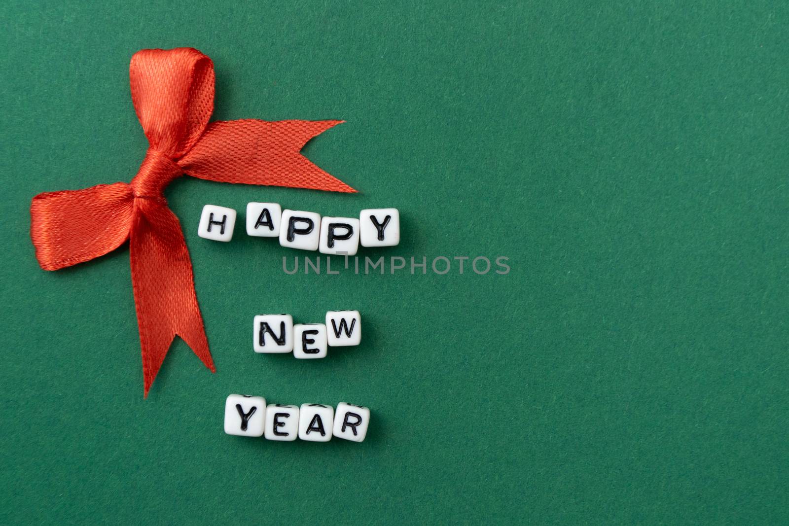 New Year concept - inscription "Happy New Year" on plastic blocks and a red Christmas bow. On a green background. Mockup for a postcard. Template for design. Copy space. Flat lay.