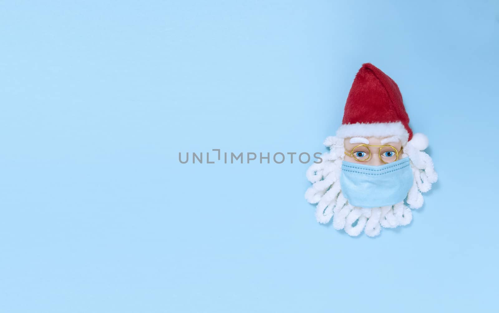 Santa Claus in medical mask on blue paper. Simple flat lay with copy space.