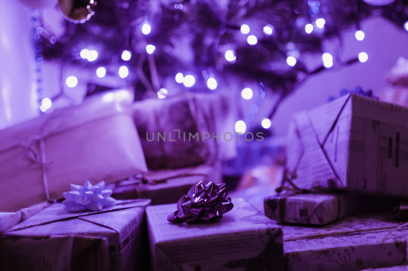 gifts packed in boxes and wrapped with festive paper with bows lie under a Christmas tree in neon light from an LED garland. The concept of winter holidays.