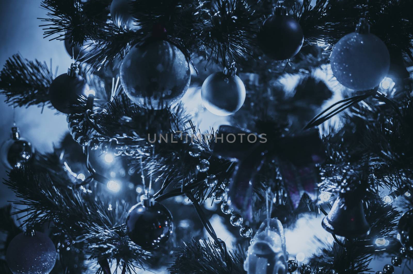 Decorated Christmas tree close-up in neon blue light. Toy balls and garland with lights with lanterns. New Year's baubles macro photo with bokeh. Winter holiday light decoration