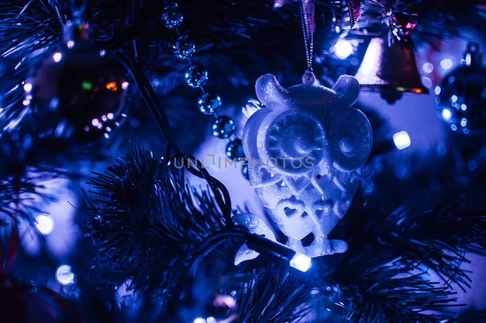 Decorated Christmas tree close-up in neon blue light. Toy glass owl and garland with lights with lanterns. New Year's baubles macro photo with bokeh. Winter holiday light decoration by Alla_Morozova93