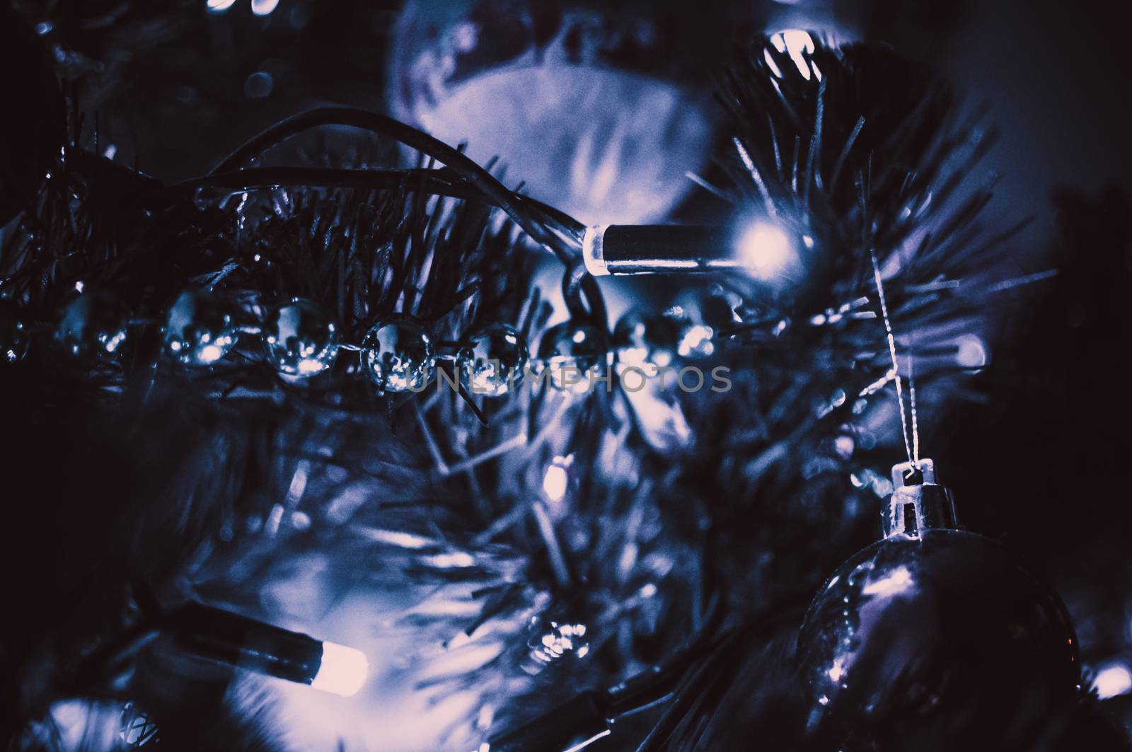 Decorated Christmas tree close-up in neon blue light. Toy balls and garland with lights with lanterns. New Year's baubles macro photo with bokeh. Winter holiday light decoration