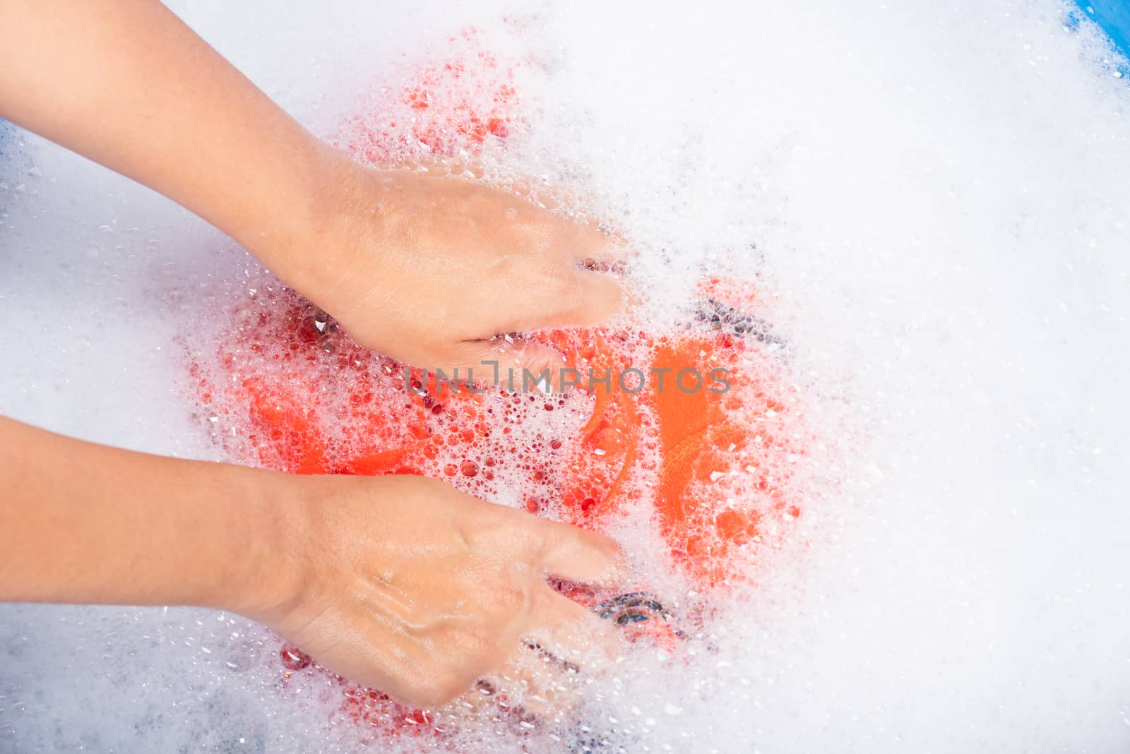 Closeup young Asian woman use hands washing color clothes in basin with detergent have soapy bubble water, studio shot background, laundry concept