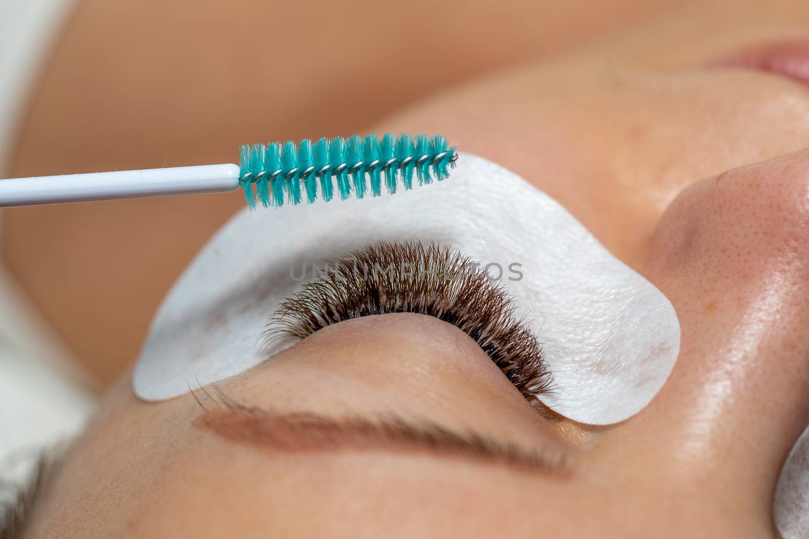 Close Woman Eye with Eyelashes Extension with eyepatch under eye and brush for care after beauty treatment closeup stock photo