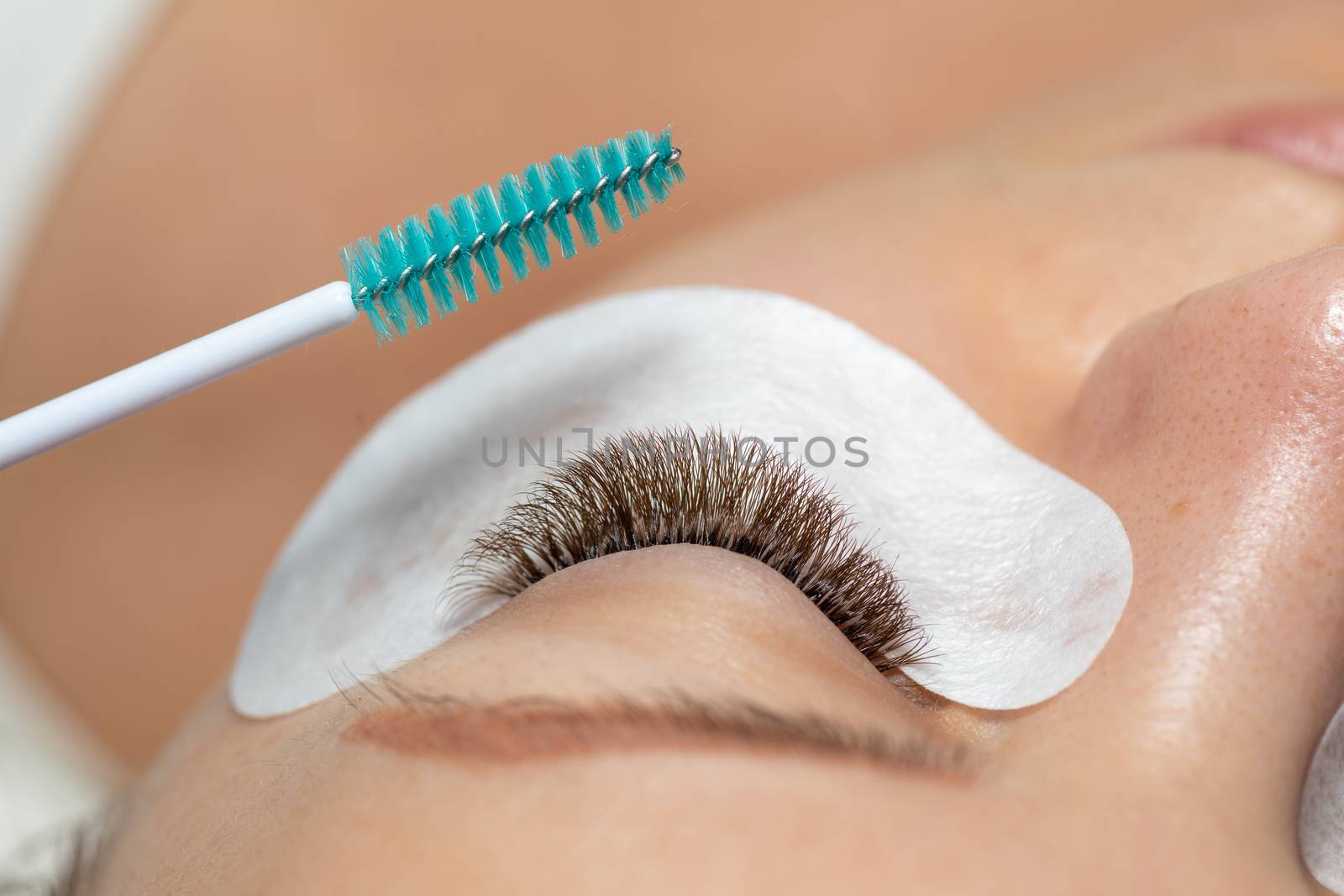 Close Woman Eye with Eyelashes Extension with eyepatch under eye and brush for care after beauty treatment closeup stock photo