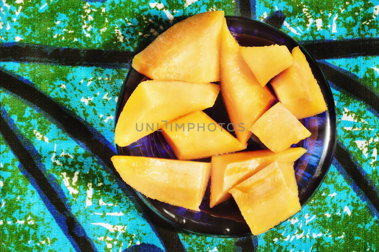 Several pieces of orange muskmelon on colored cloth background , fruit pieces are in a blue bowl