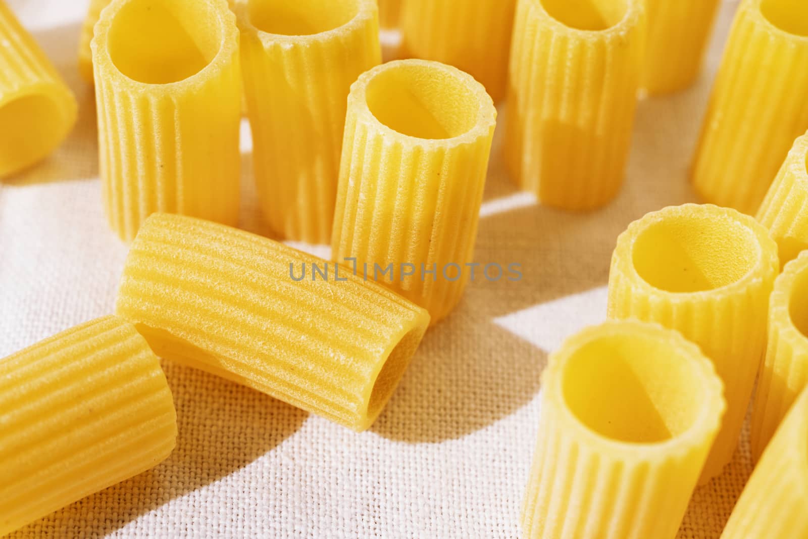 Italian pasta called mezzi rigatoni on white cotton cloth ,tube-shaped pasta with ridges down their lenght ,studio shot