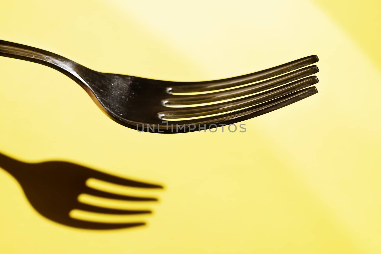 Part of one fork against yellow background , beautiful fork shadow on the background 