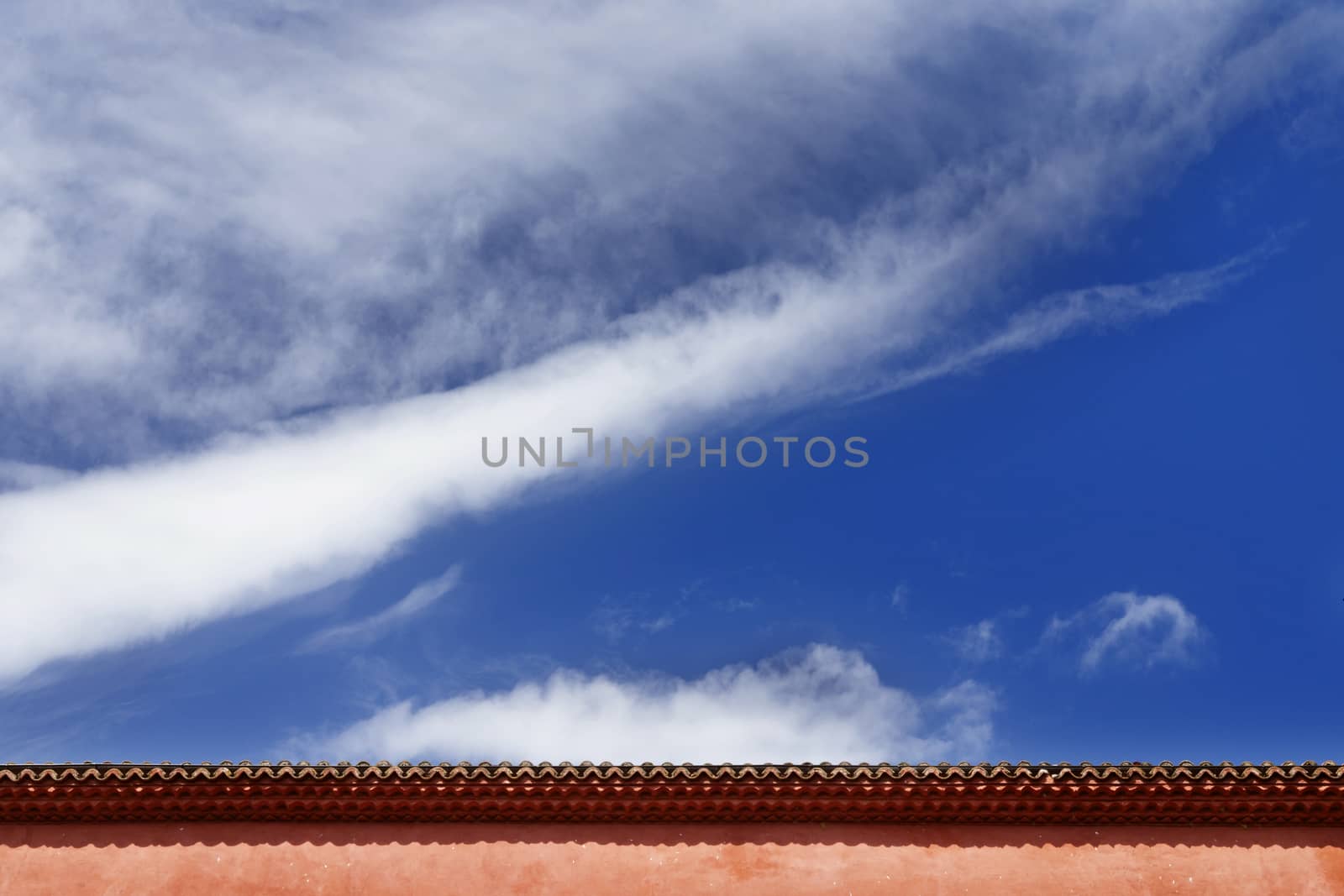 Beautiful cloudy sky in a bright sunny day , part of roof and red outer wall of a house