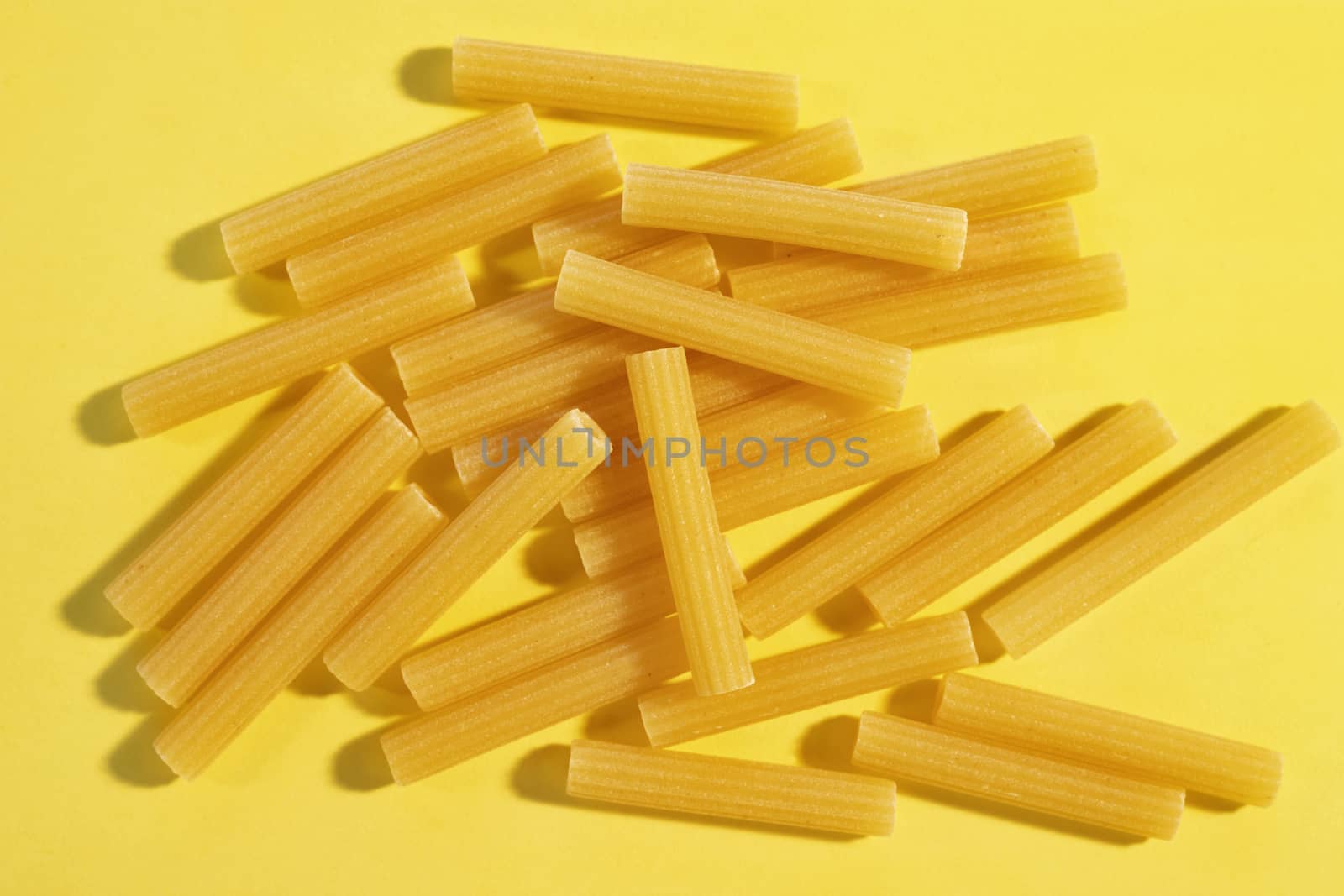 Dry pasta called maccheroni or maccaroni shaped like narrow tubes on colored background