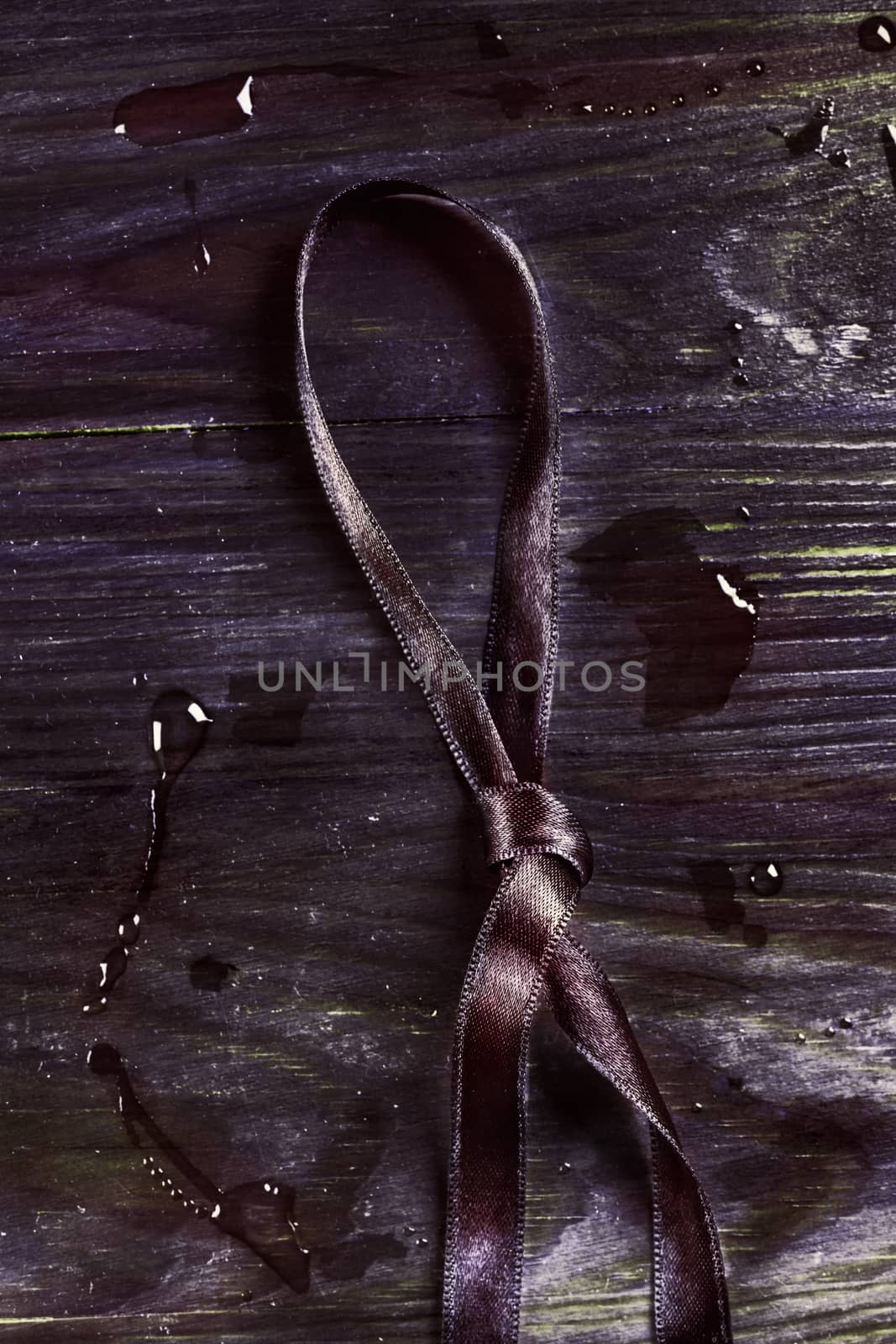 Dark purple and knotted  ribbon on wooden background ,  several bright  water drops on the background