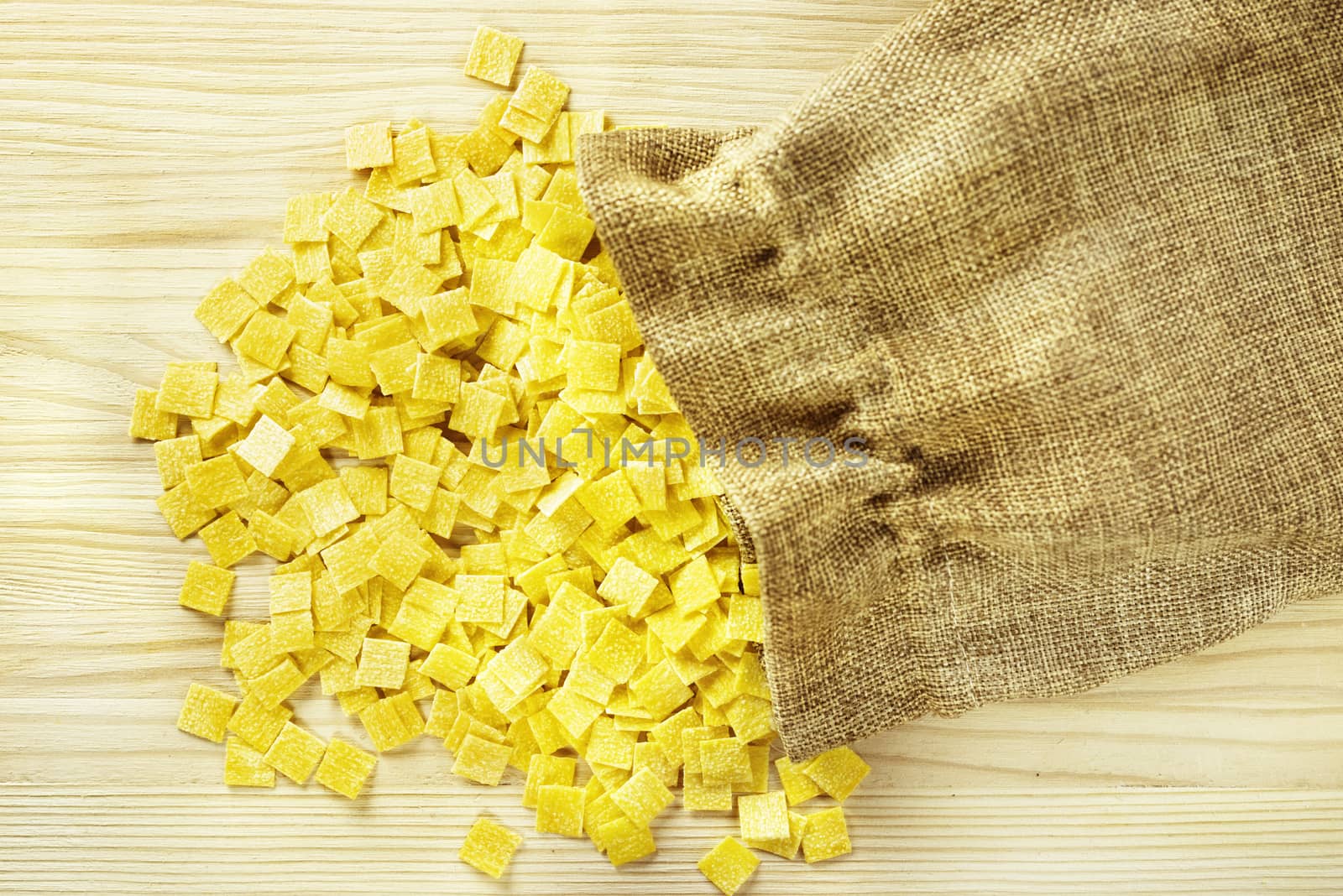 Pile of small flat squares of egg pasta called quadrucci  sackcloth bag,yellow color pasta with rough surface 