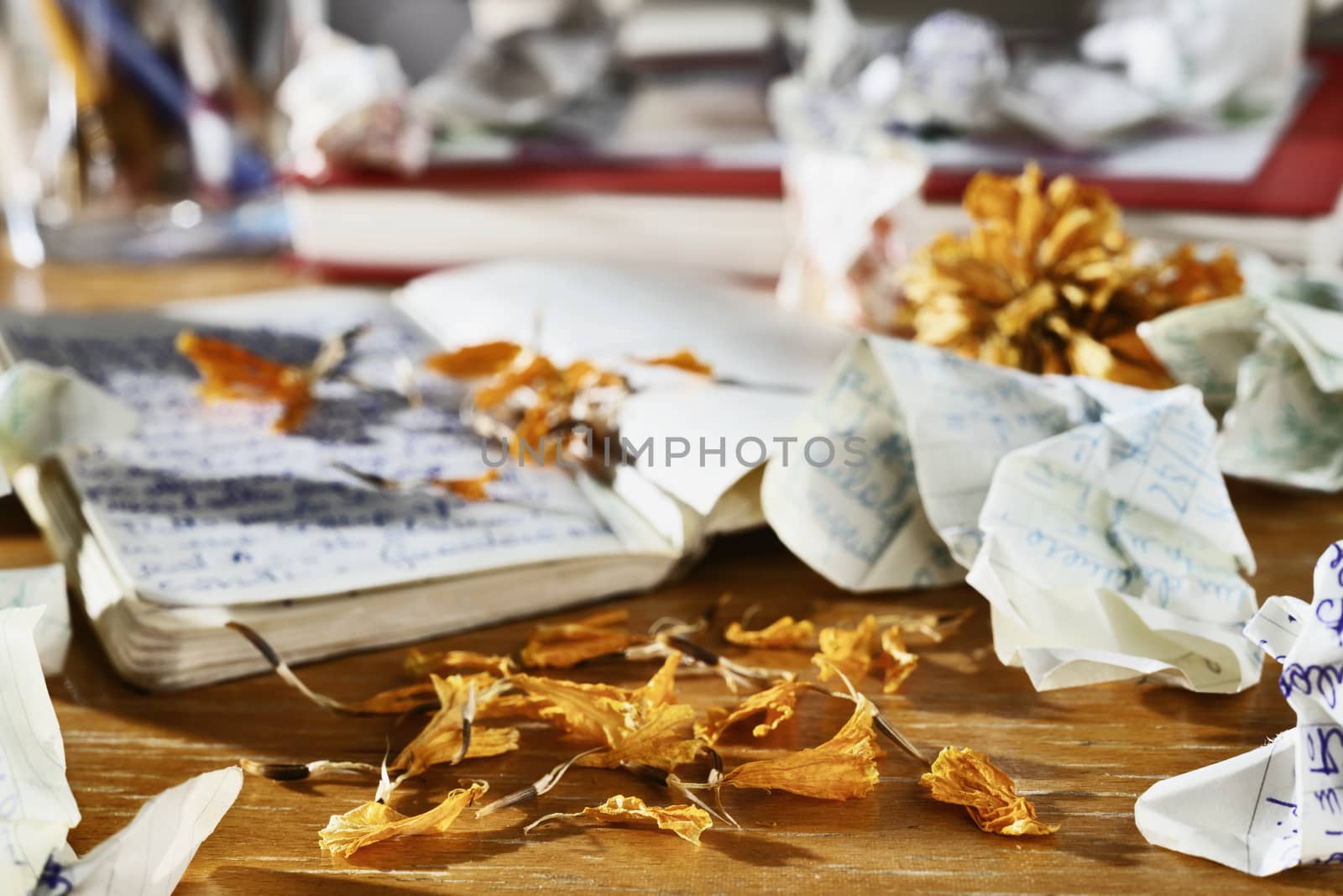                                                                                                                                                                                                                                                                                                                                                                                                                                                                                                                 Open diary book with written crumpled  papers and dry orange flower petals on wooden table next an opened diary ,in the background books , pencil box and crumpled papers , relationship crisis