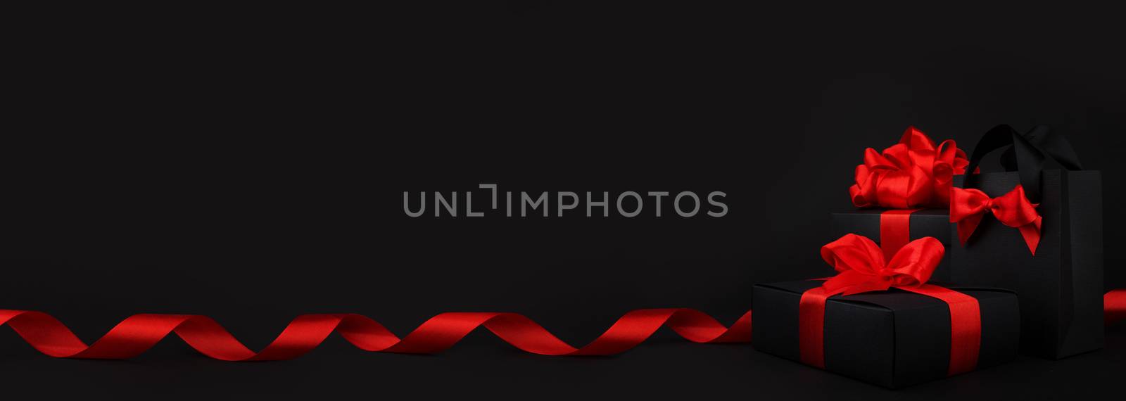 Gift box wrapped in black paper with red ribbon on black background, design banner black friday sale concept copy space for text