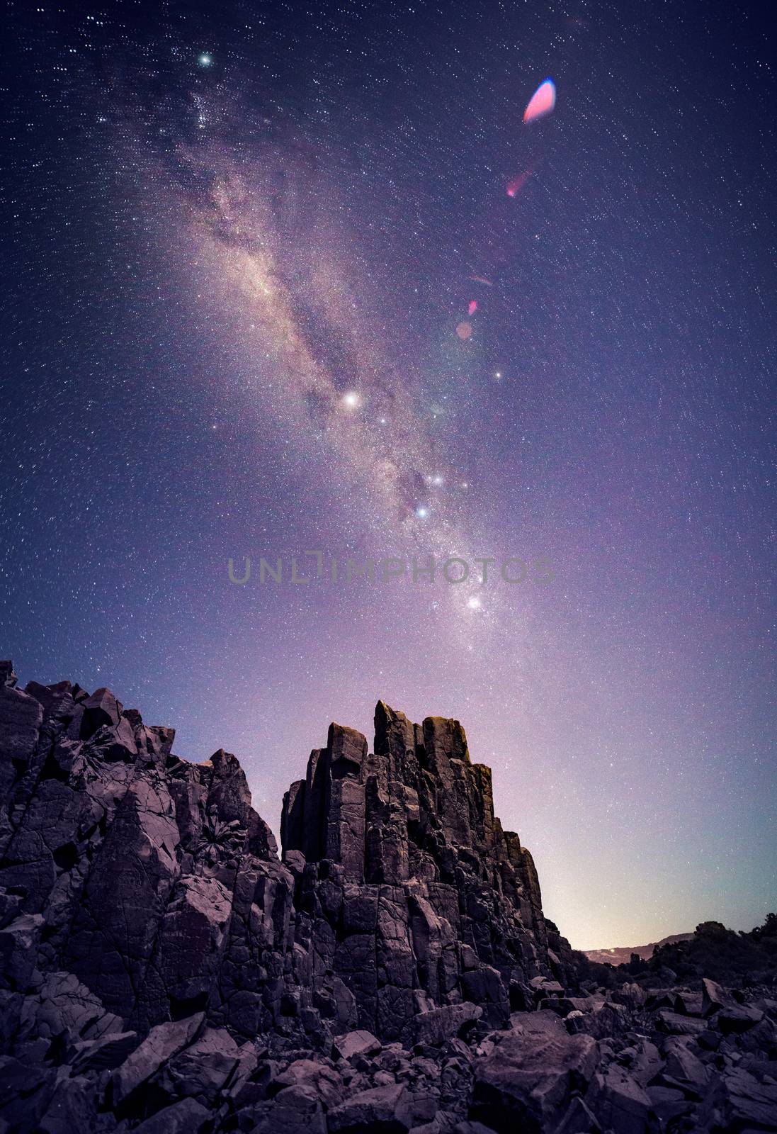 Granite column rocks under a starry night sky with lens flare and glow from nearby suburb