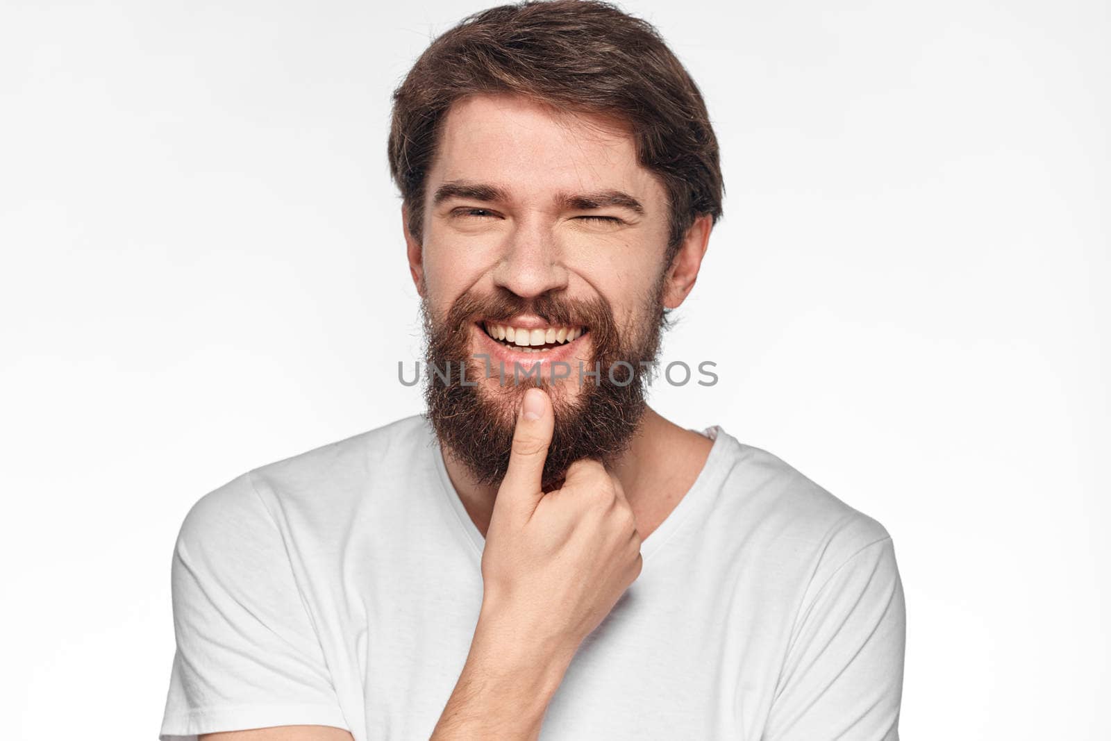 cheerful bearded man in a white t-shirt emotions gestures with his hands light background studio. High quality photo