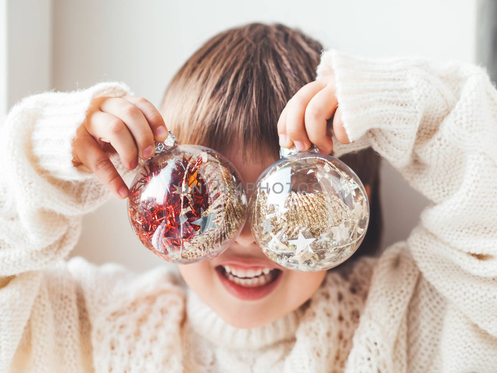 Kid with decorative balls for Christmas tree.Boy in cable-knit oversized sweater.Cozy outfit for snuggle weather.Transparent balls with red, golden spangles inside.Winter holiday spirit.New year.