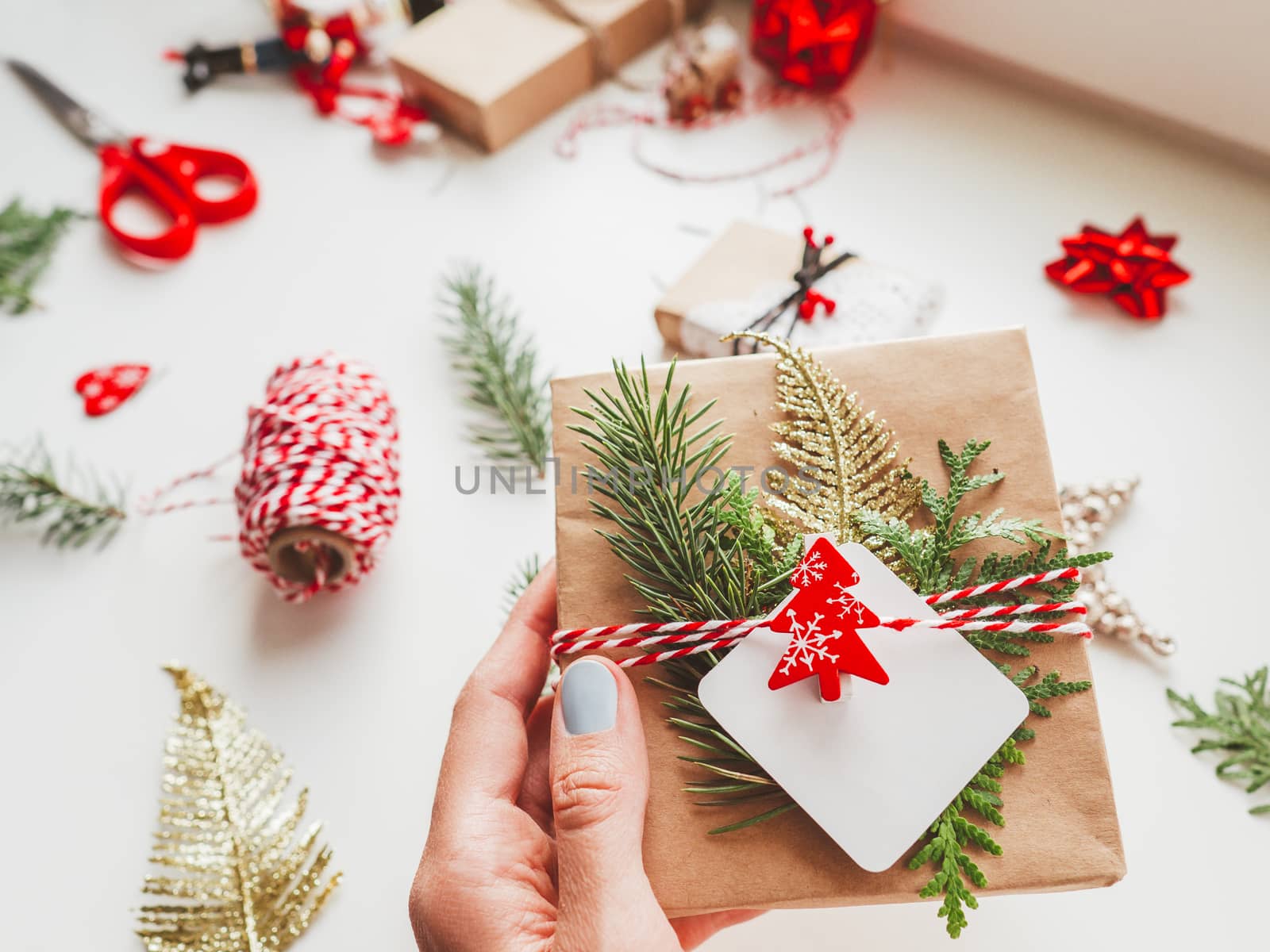 DIY presents wrapped in craft paper with fir tree twigs and red symbol of Christmas tree. Top view on decorations on New Year gifts. Festive background. Winter holiday spirit.