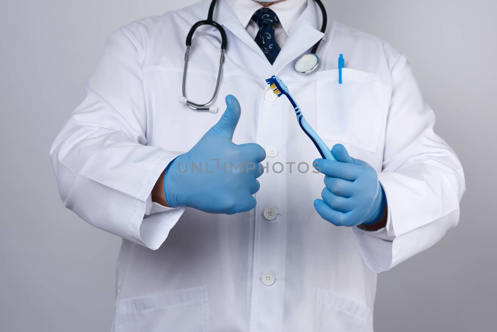 doctor therapist is dressed in a white robe uniform and blue sterile gloves is standing and holding a toothbrush, daily brushing concept, white background