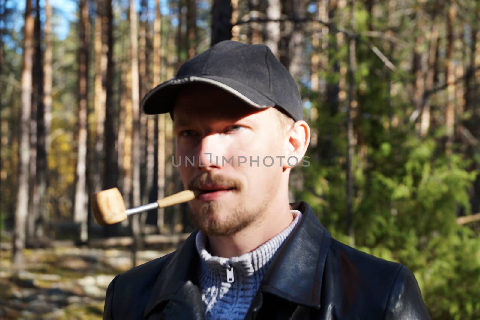 young man in a cap smokes a pipe in the forest by Annado