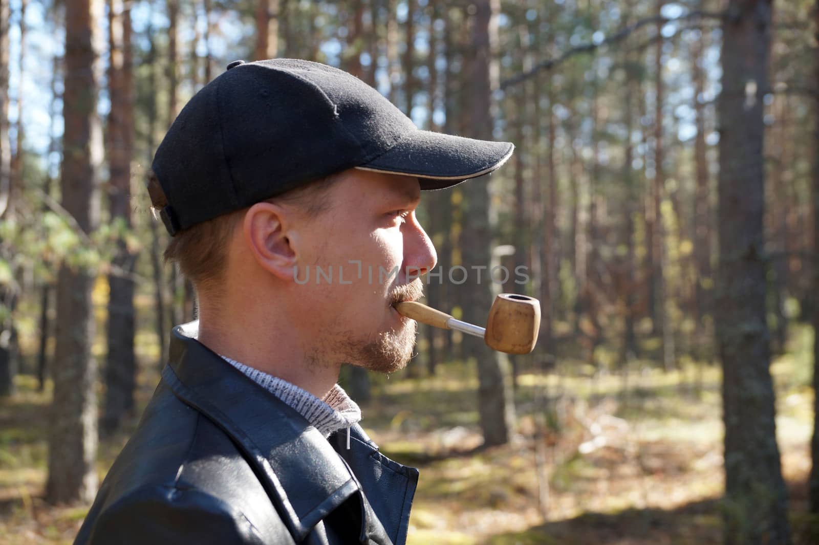 young man in a cap smokes a pipe in the forest by Annado