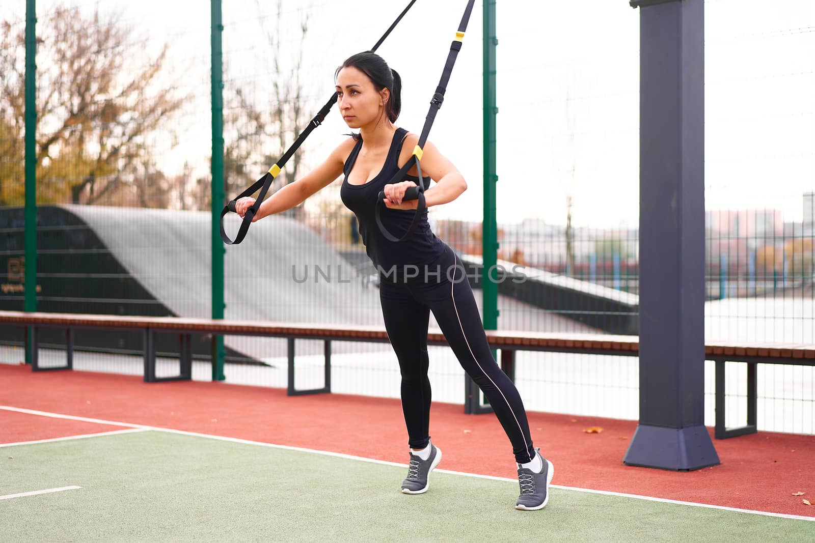 Girl athlete training using trx on sportground. Mixed race young adult woman do workout with suspension system. Healthy lifestyle. Stretching outdoors playground. by andreonegin