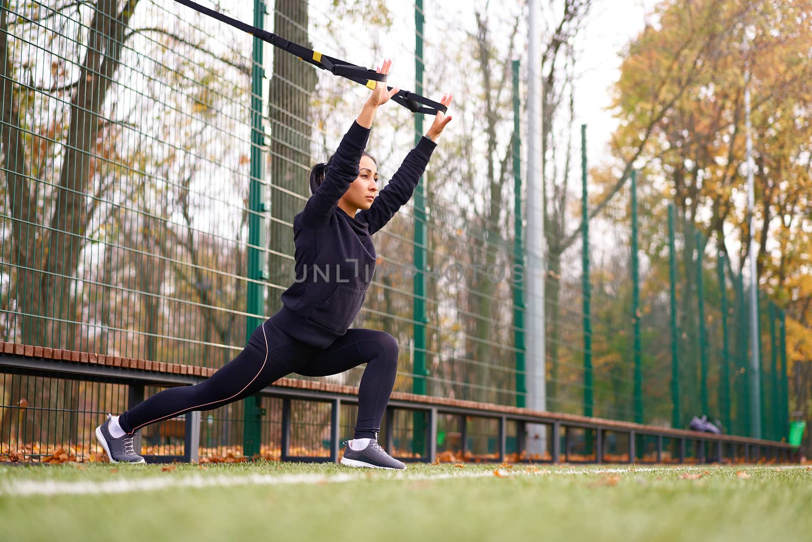 Girl athlete training using trx on sportground. Mixed race young adult woman do workout with suspension system. Healthy lifestyle. Stretching outdoors playground. by andreonegin