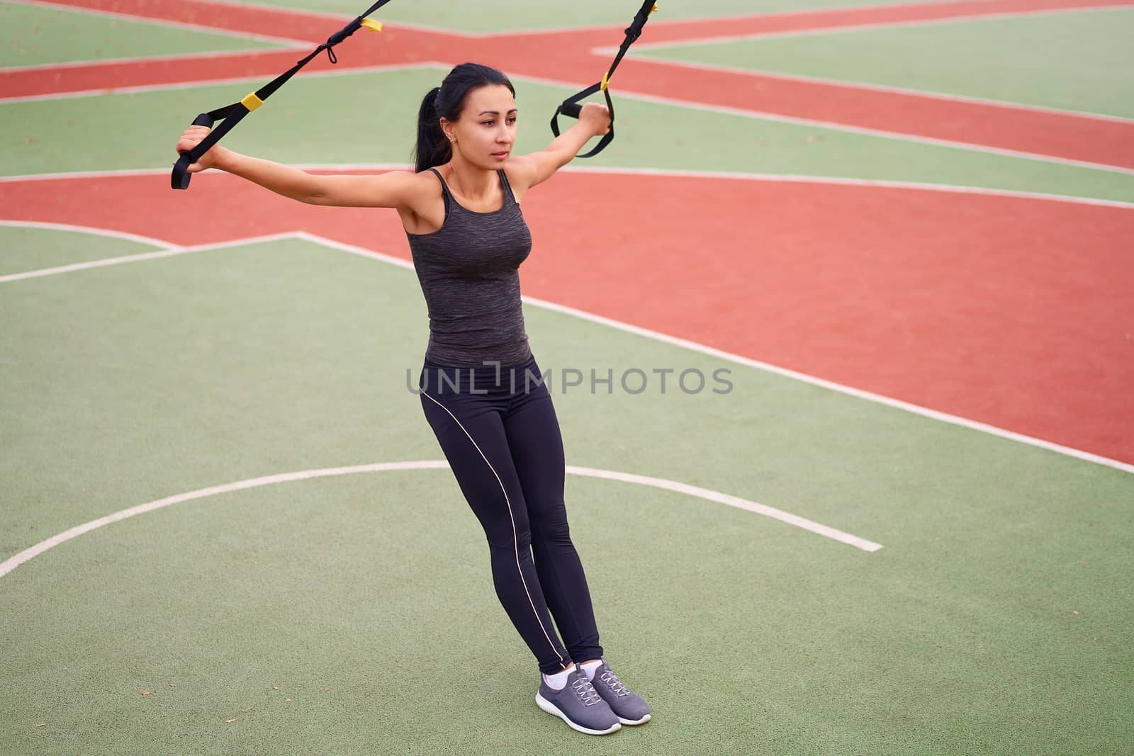 Girl athlete training using trx on sportground. Mixed race young adult woman do workout with suspension system. Healthy lifestyle. Stretching outdoors playground. by andreonegin