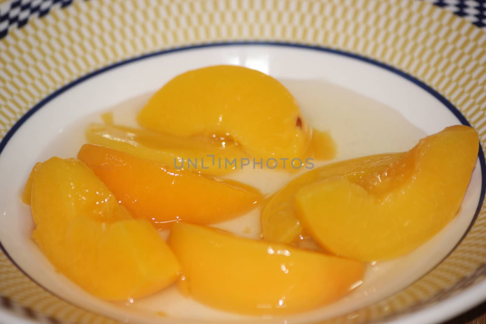 Closeup high angle view with selective focus of yellow peaches slices. Canned peaches halves sprinkled with syrup in white plate.