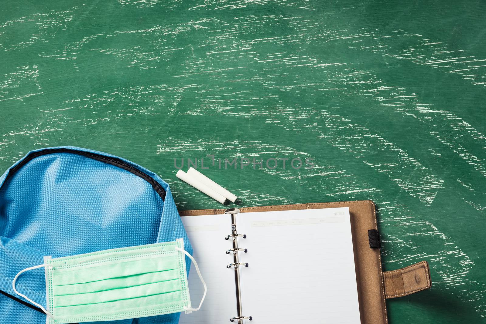 Top view of blue school bag backpack at a green chalkboard with face mask protection and have copy space for your text, Back to school education during epidemic coronavirus concept