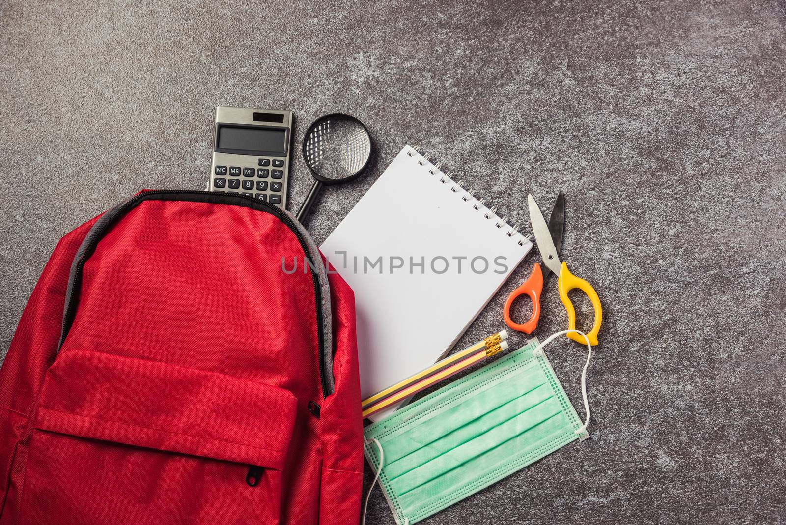 Top view of stylish red school bag backpack on a table desk with face mask protection and stationery, Back to school education new normal during outbreak COVID-19 or coronavirus concept