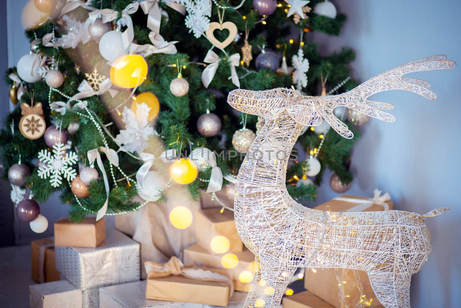 A festive decorative deer stands in the room against the background of a Christmas tree and a mountain of gifts. Gifts for the new year under the tree. Holiday atmosphere