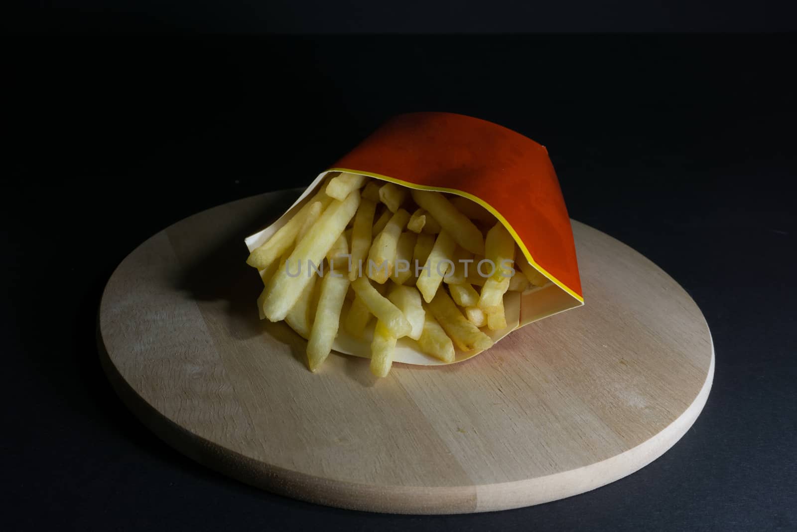 French fries on a black background on a wooden board in a red and yellow package