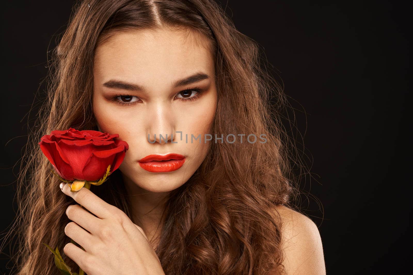 woman with a red rose on a dark background long hair makeup red lips. High quality photo