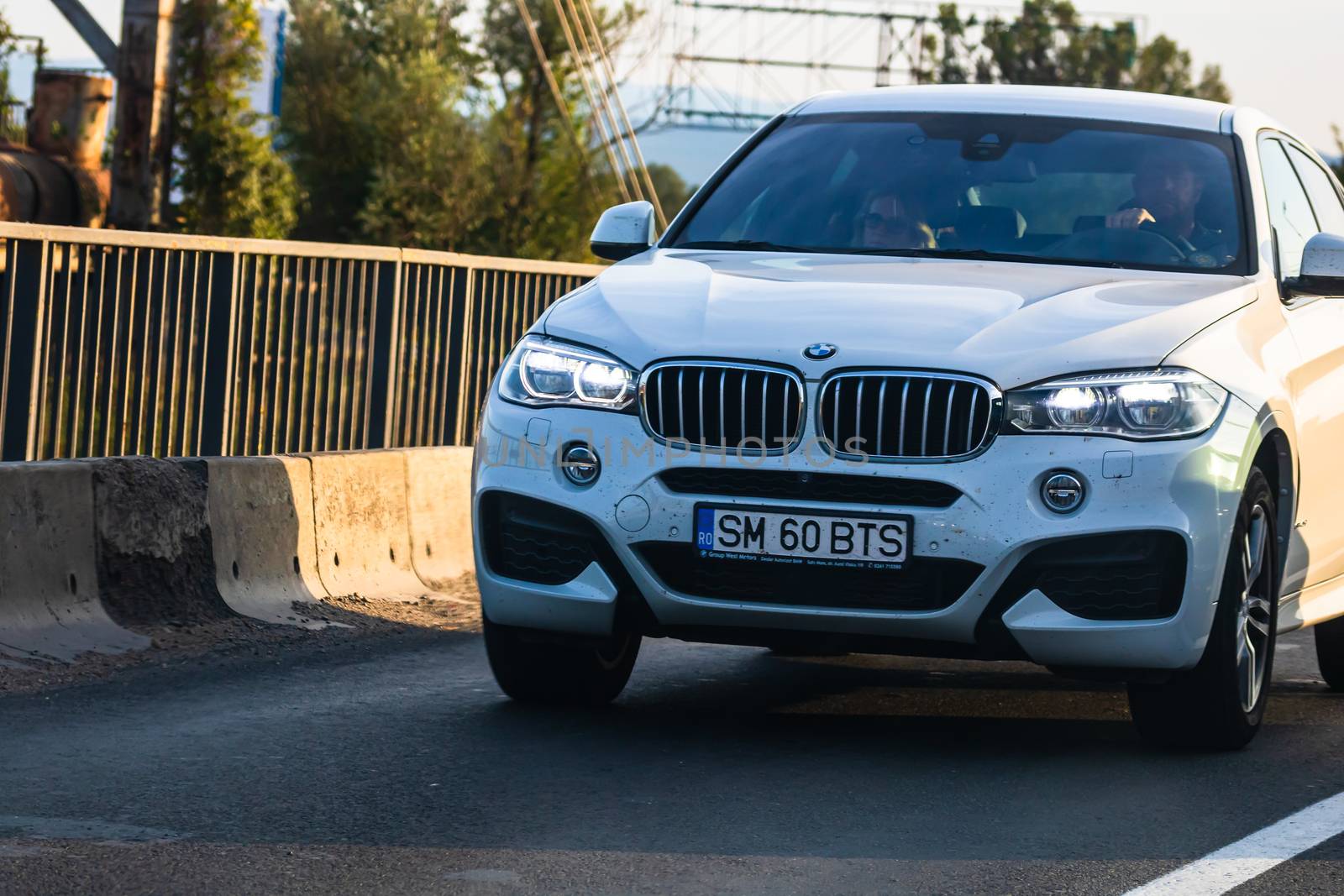 Traveling white BMW car in motion on asphalt road, front view of by vladispas