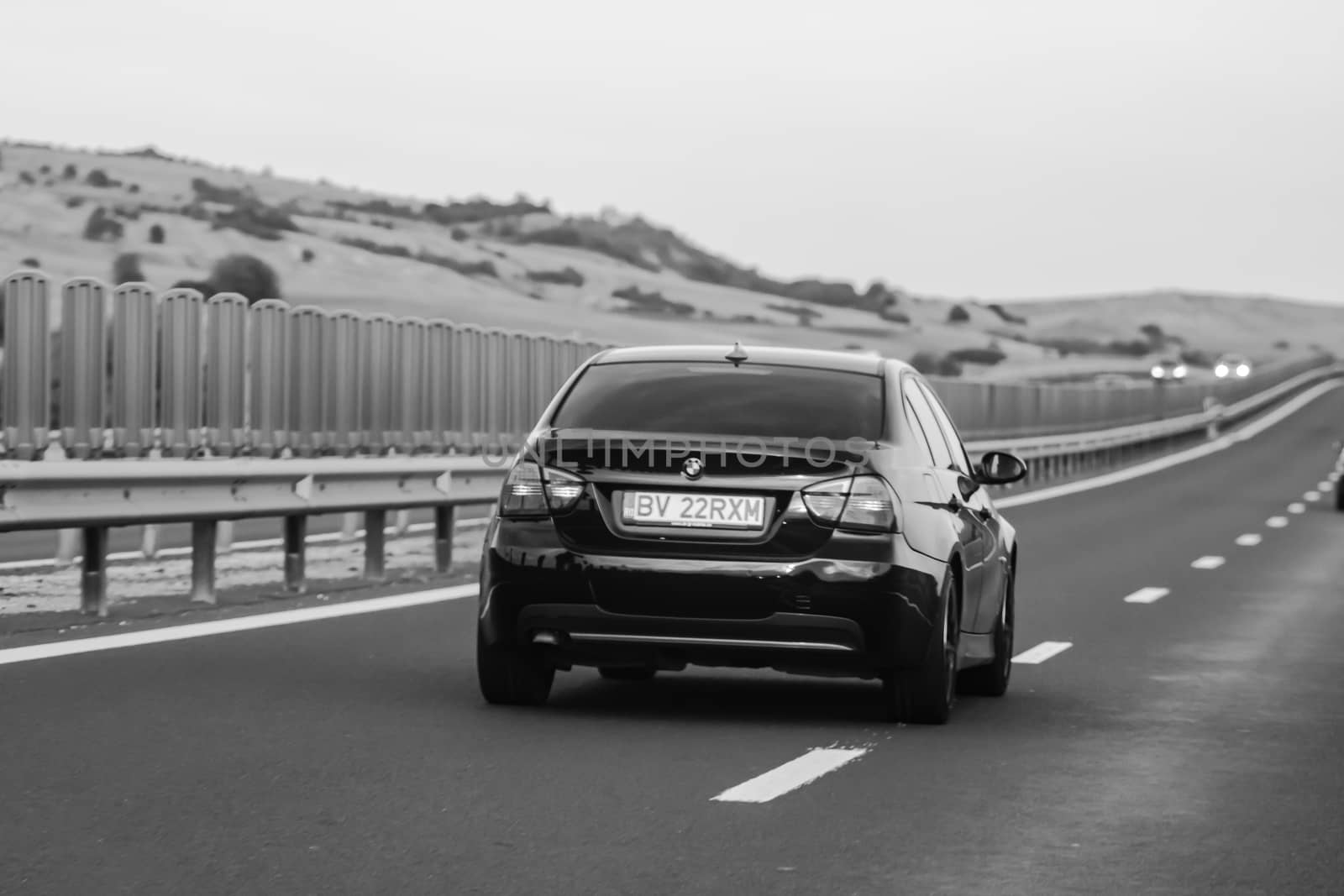 Traveling black car in motion on asphalt road, back view of car  by vladispas