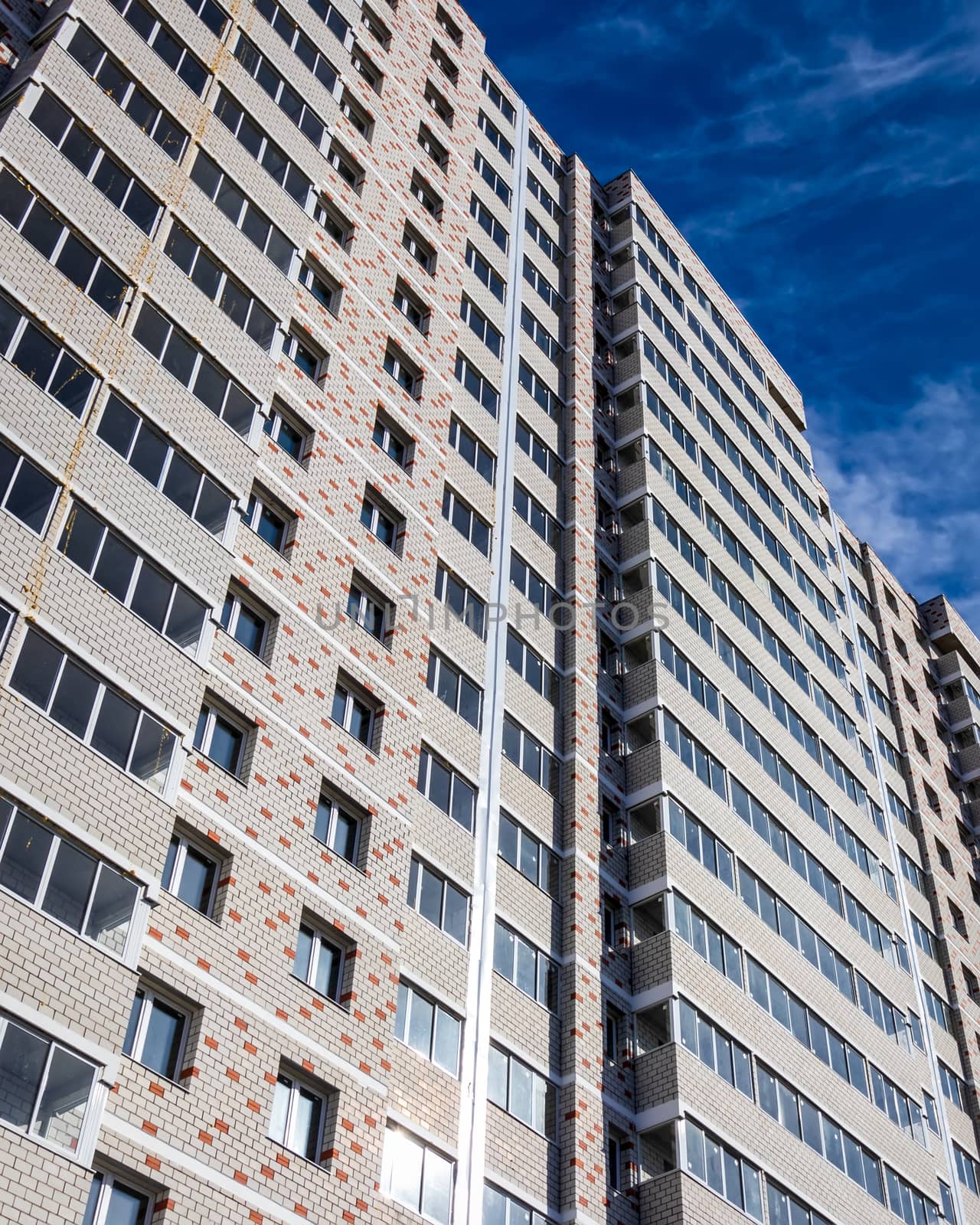 Fragment of a white brick residential building with balconies against a clear sky.