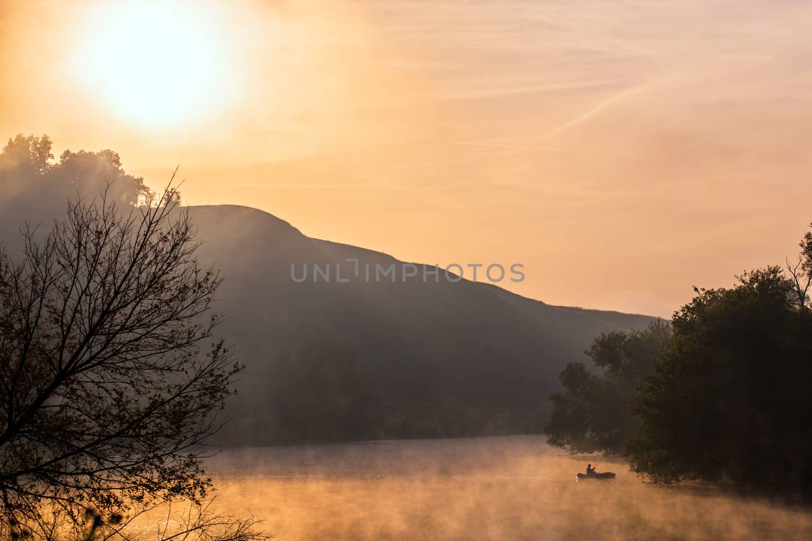 Silhouette of a fisherman in a boat on a foggy river in the morning