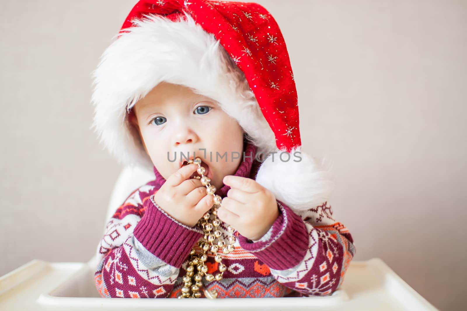 A little baby girl in a New Year's hat of Santa Claus examines and plays with New Year's decorations. by malyshkamju
