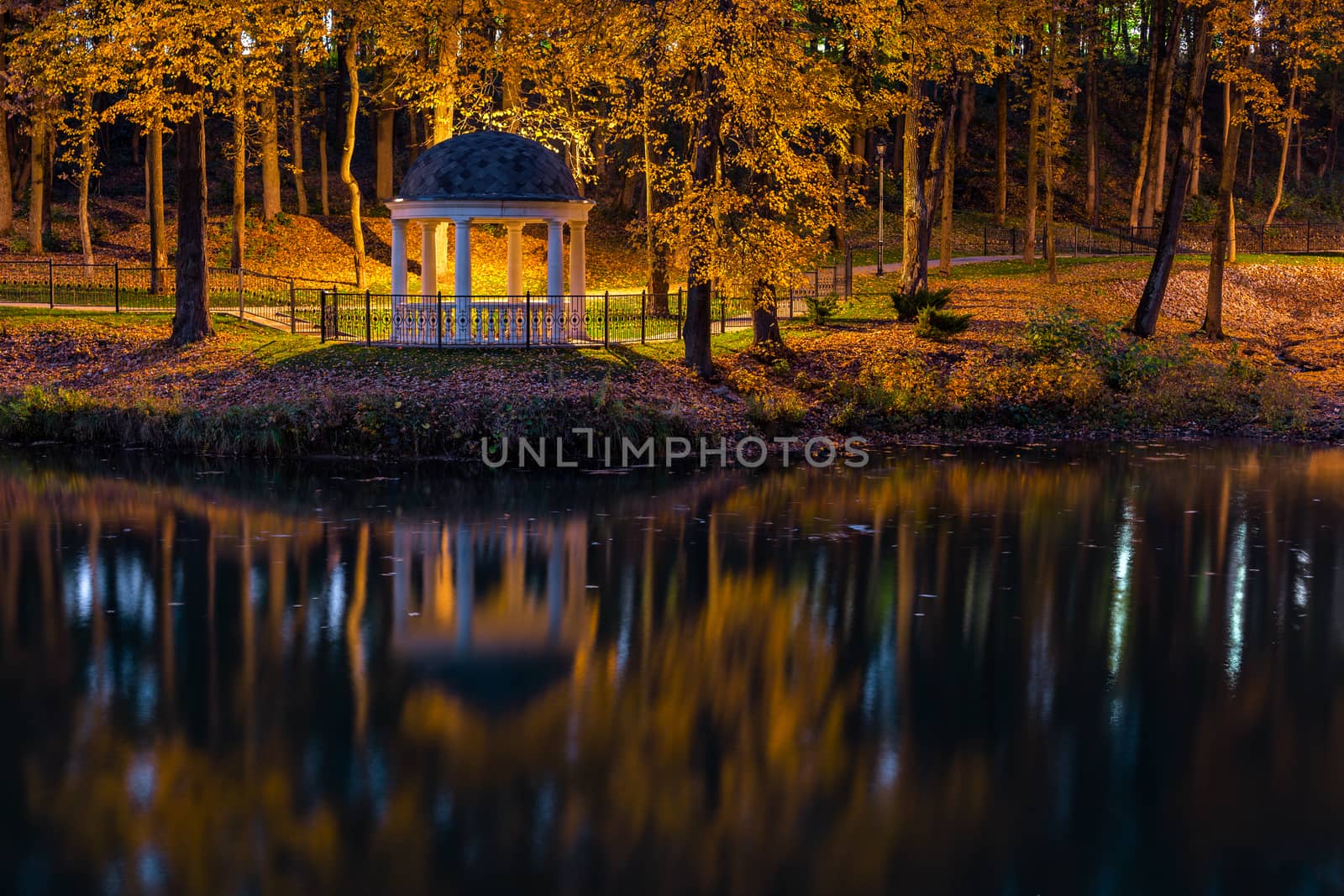 Night in autumn park with pond and white rotunda