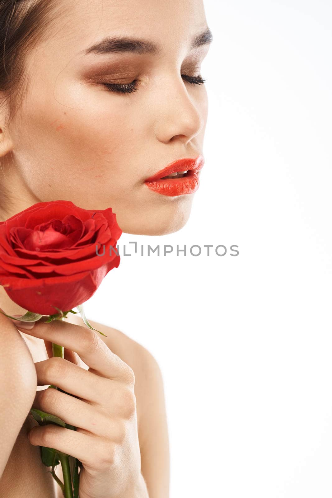 Beautiful woman with red rose near face makeup naked shoulders portrait. High quality photo