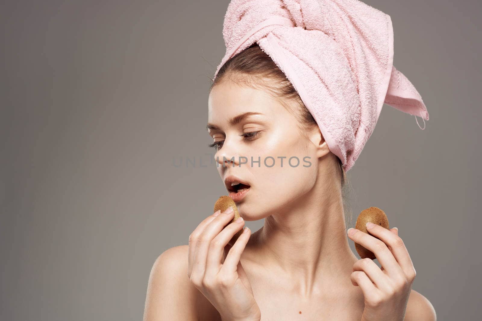 beautiful woman with pink towel on her head naked shoulders kiwi in hands health skin care. High quality photo