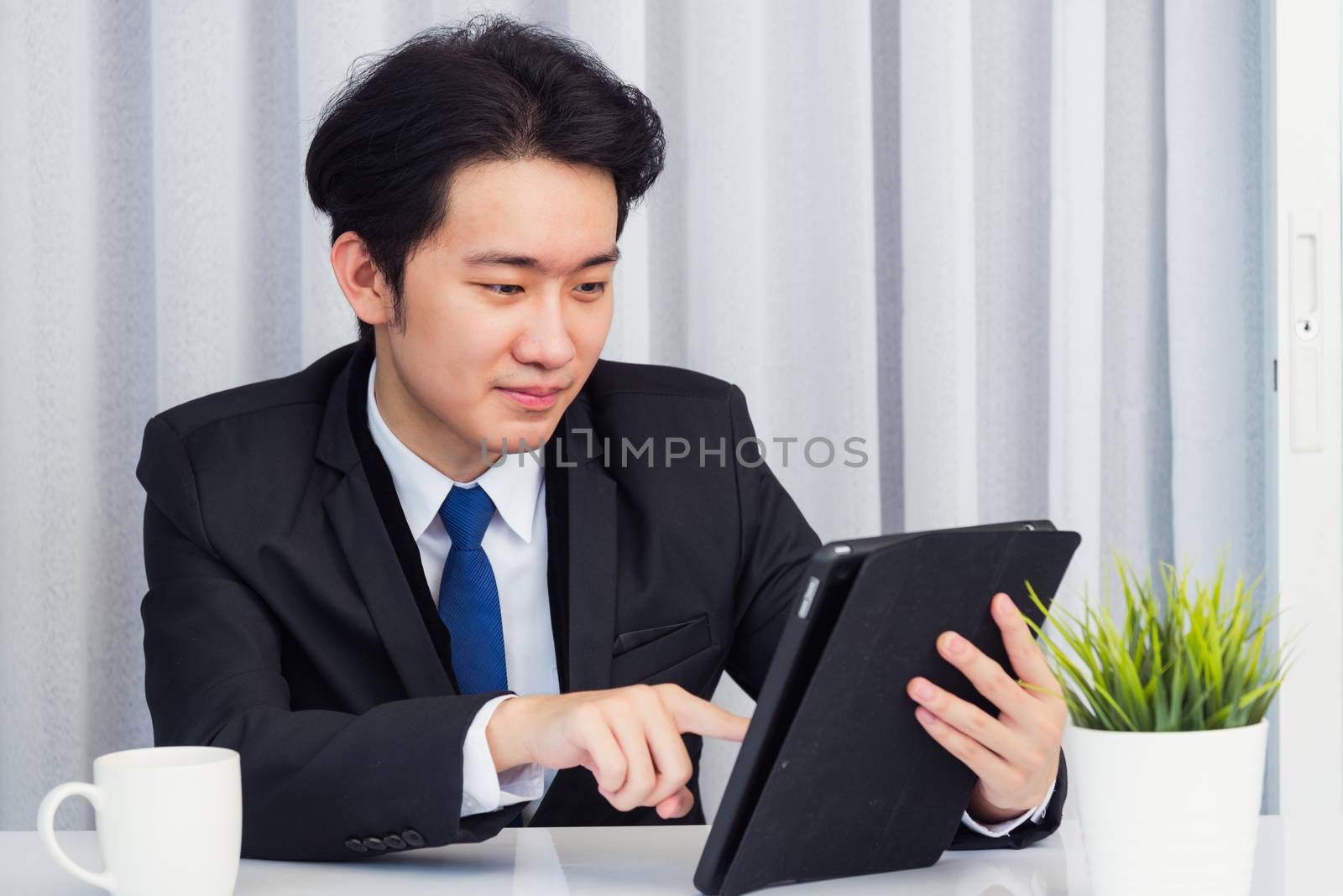 Work from home, Asian young businessman video conference call or facetime he smiling looking to camera sitting on desk using smart digital tablet computer touching on screen at home office