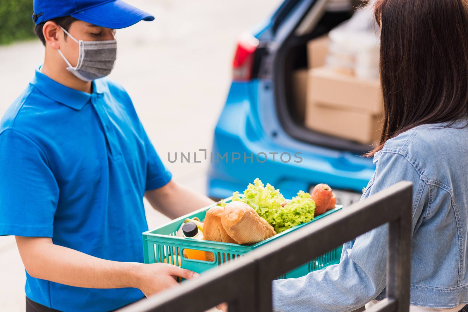 Asian young delivery man wear face mask making grocery fast service giving fresh food vegetable in plastic basket to woman customer receive at house door after pandemic coronavirus, Back to new normal