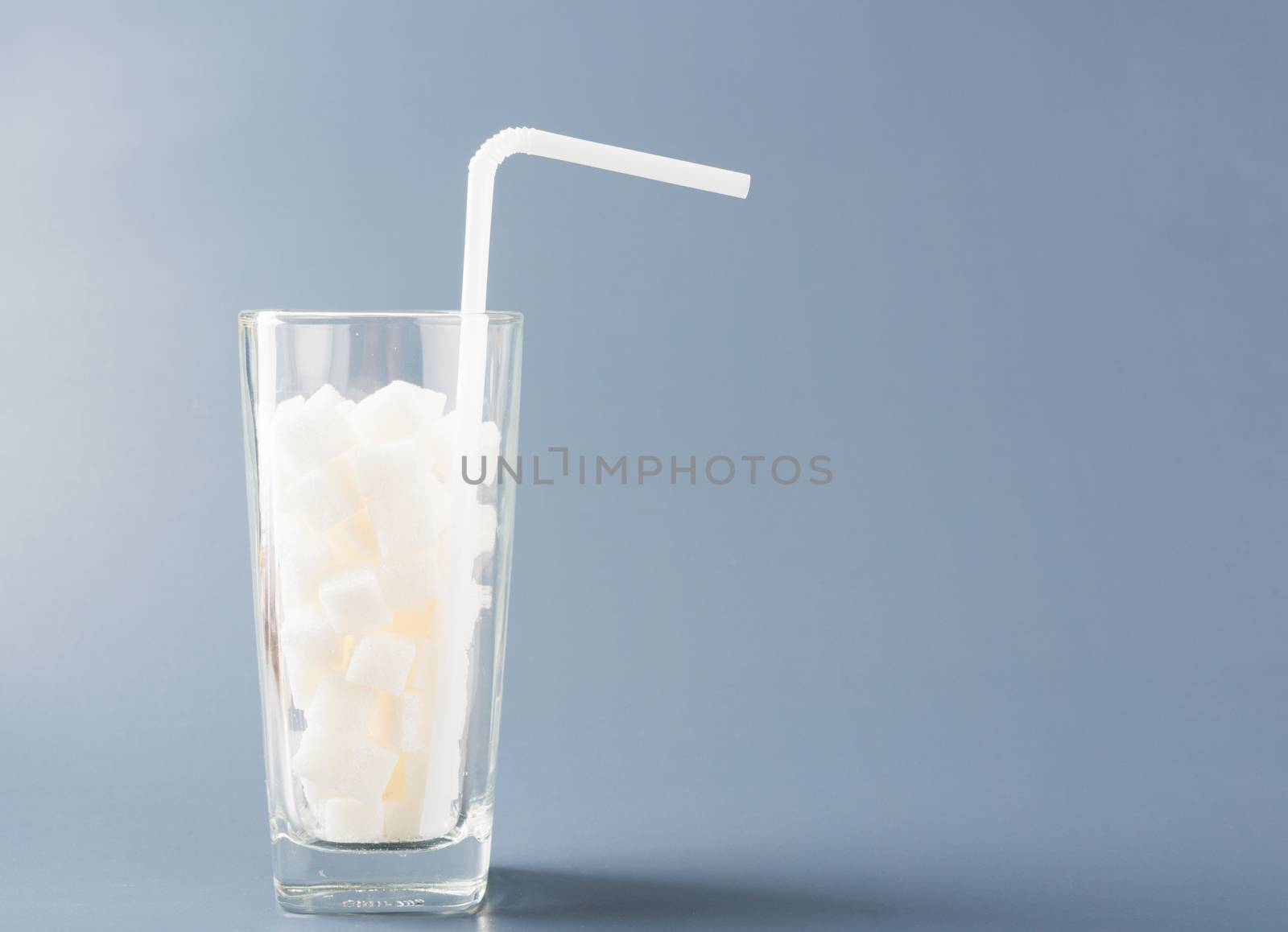 A glass full of white sugar cube sweet food ingredient, studio shot isolated on a gray background, health high blood risk of diabetes and calorie intake concept and unhealthy drink