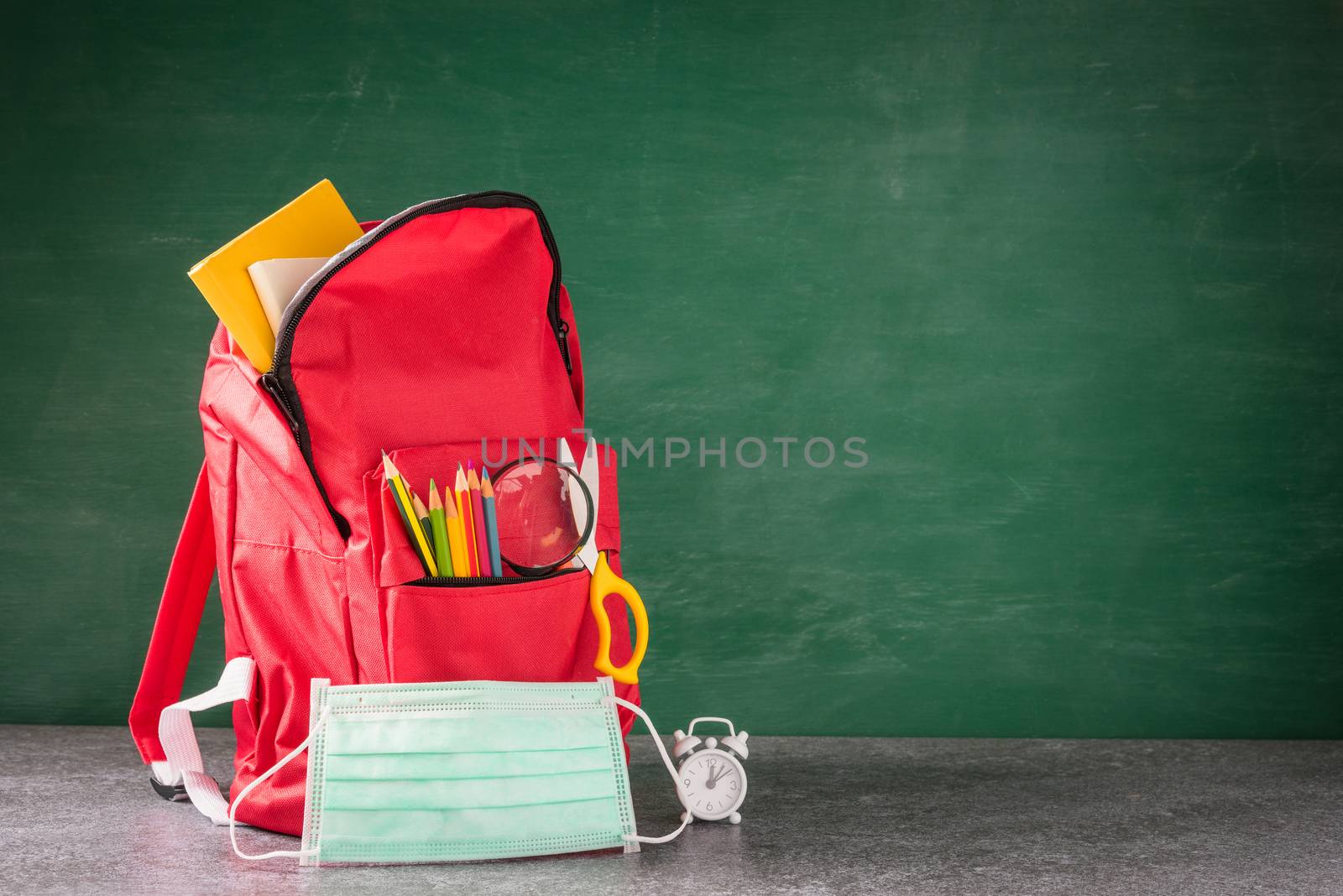Front school backpack and accessories with face mask protect on desk at green chalkboard, student bag at classroom backboard, Back to school education new normal outbreak COVID-19 or coronavirus