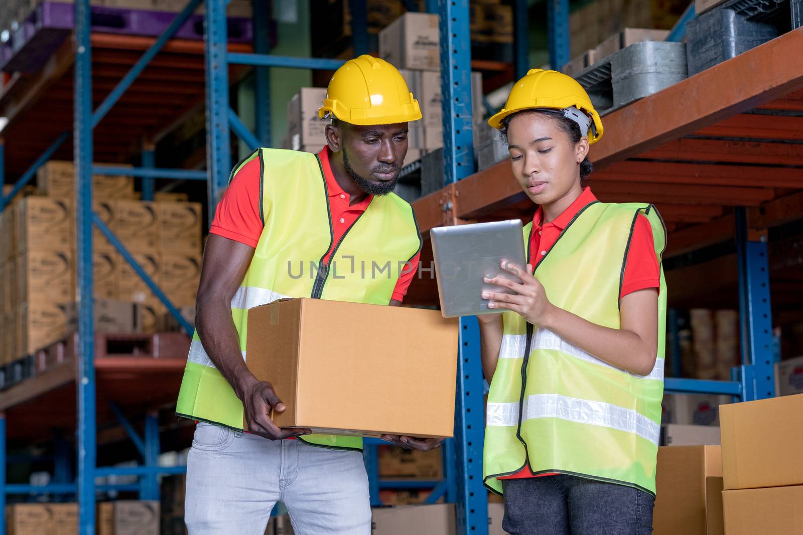 African American warehouse man and woman or factory worker work and discuss together about product box that man holding in workplace area. Concept of good management of staff working.