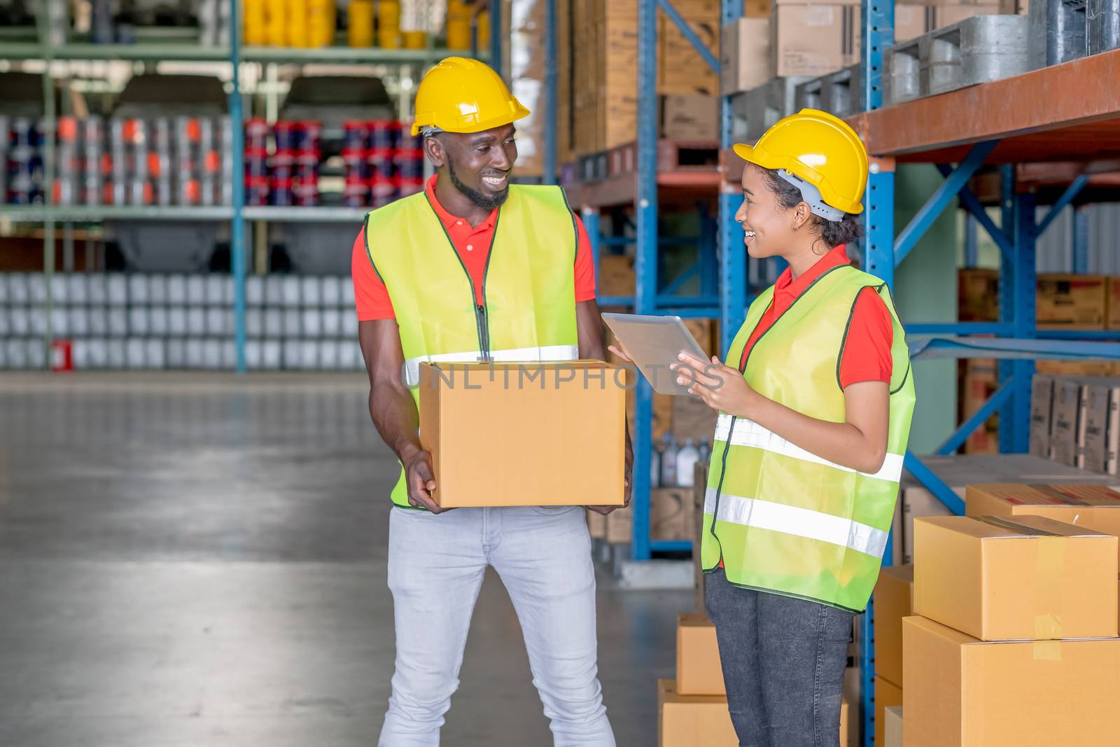 African American warehouse man and woman or factory worker work and discuss together about product box that man holding in workplace area. Concept of good management of staff working.